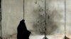 Iraq -- Two Iraqi women walk past cement blast walls scared by a detonated road side bomb which targeted a police patrol in the Karada district of the capital Baghdad, 13Jul2009