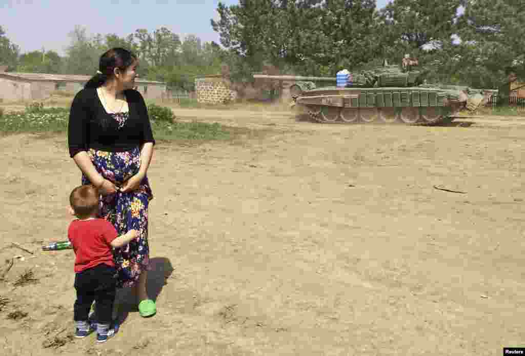 Жінка з дитиною спостерігає за пересуванням військової техніки. Конвой їде на полігон Кузьмінський – тренувальну військову базу на кордоні Росії та України. 26 травня 2015 року