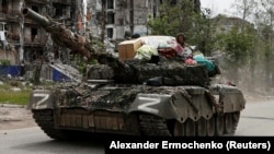 Rusiye arbiyleri Lugansk vilâyetiniñ Popasna şeerinde evden hırsızlanğan mallarnen tankta bulunalar. 2022 senesi mayısnıñ 26-sı