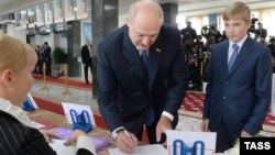 Баласы Николайды (оң жақта) ертіп Беларусь президенті сайлауына дауыс беруге келген елдің қазіргі президенті Александр Лукашенко (ортада) сайлау учаскесінде дауыс беру бюллетенін алып тұр. Минск, 11 қазан 2015 жыл.