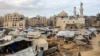 A man carries a jerrycan as he walks past tents sheltering people displaced by war pitched near the heavily-damaged Sheikh Hamad bin Khalifa Al-Thani mosque at the Qatari-built Hamad City residential complex in northwestern Khan Yunis, in the southern Gaz